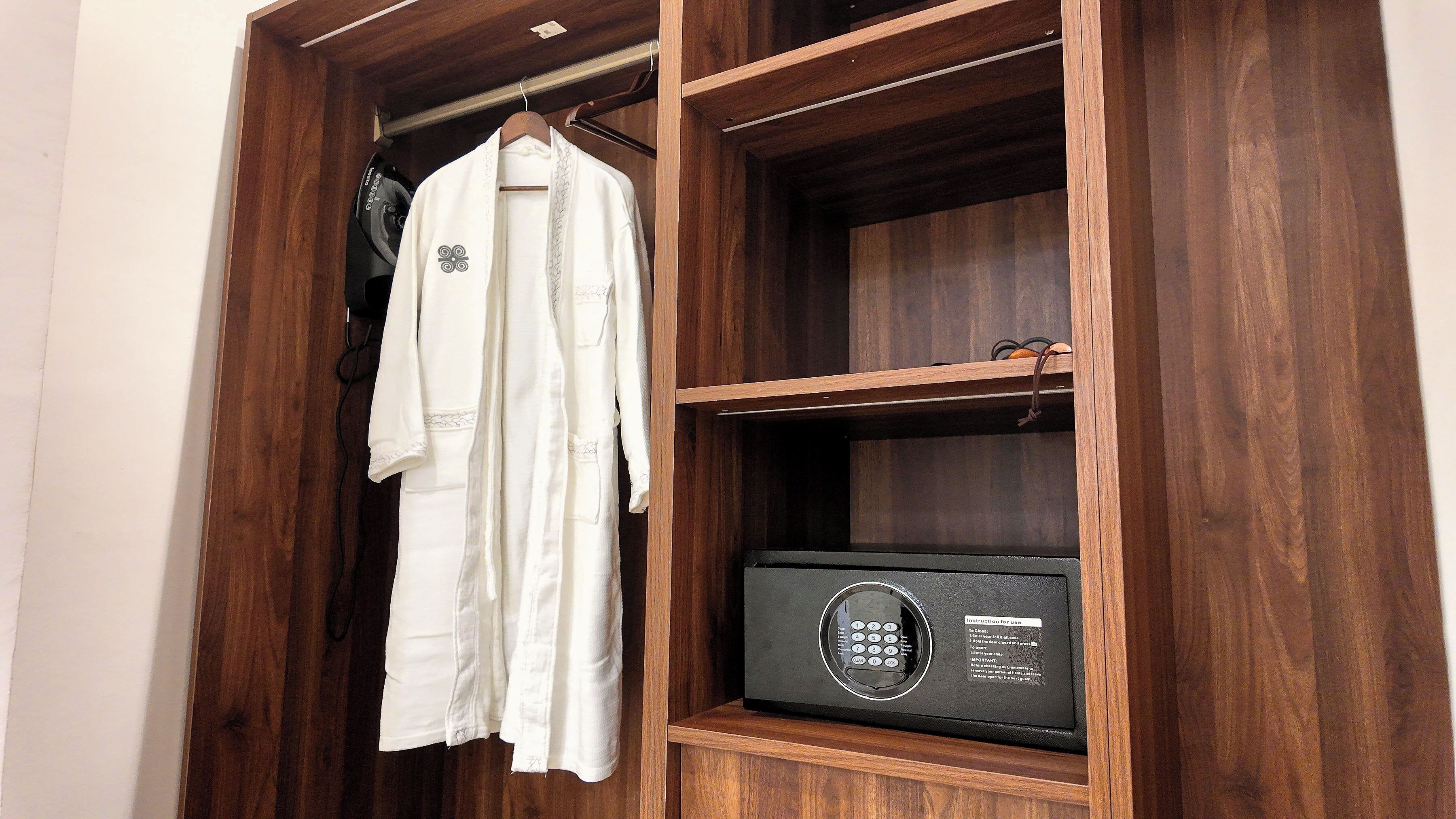 Une armoire en bois dans laquelle est suspendue une robe blanche sur un cintre, et à l’intérieur, un four à micro-ondes noir.