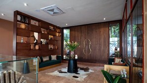 Un interior moderno con un separador de vidrio, una estantería de madera, un sofá, una mesa de centro y una planta grande.