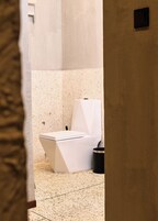 A bathroom with a white toilet, a black trash bin, and a speckled floor.