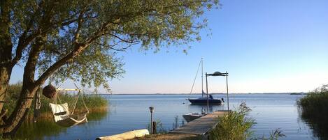A calm lake with a dock, a boat, and a hammock under a tree.