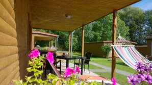 Un portico coperto con tavolo e sedie, un'amaca e un giardino fiorito.