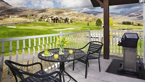 Un balcon avec une table et des chaises, un barbecue et une vue sur un terrain de golf et les montagnes.