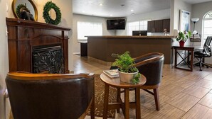 Un salon moderne avec une cheminée, des fauteuils en cuir, une table basse agrémentée d’une plante, et un coin cuisine à l’arrière-plan.