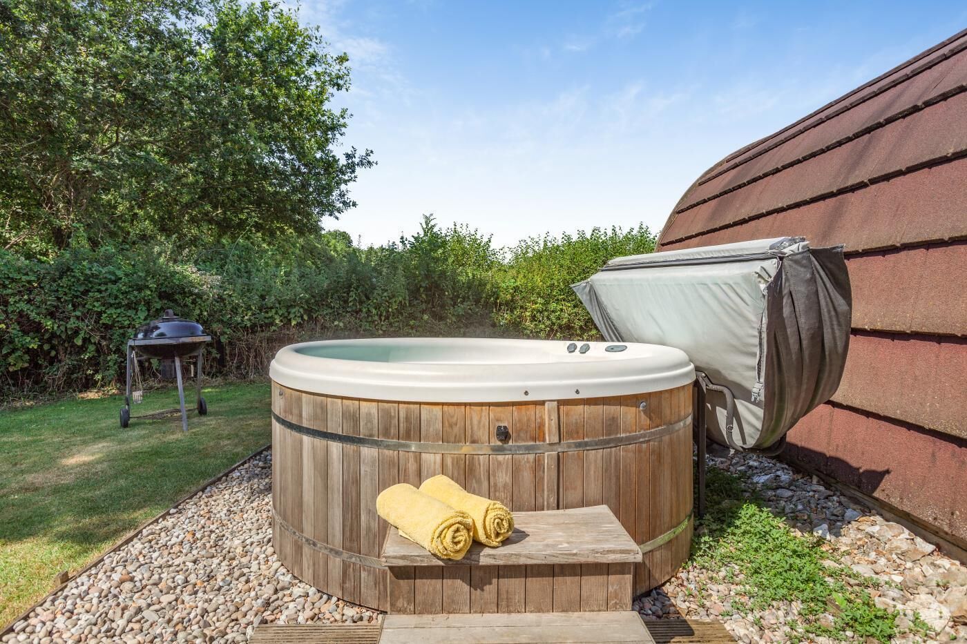 Ein hölzernes Whirlpool mit Deckel, ein Grill und ein Handtuch auf einer Stufe.