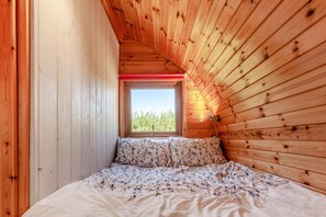 A bedroom with a sloped ceiling, wooden walls, a window, and a bed with patterned bedding.