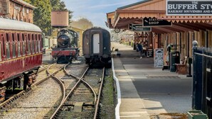 Una stazione ferroviaria con un binario, un treno d'epoca e un negozio chiamato 'The Buffer Store'.