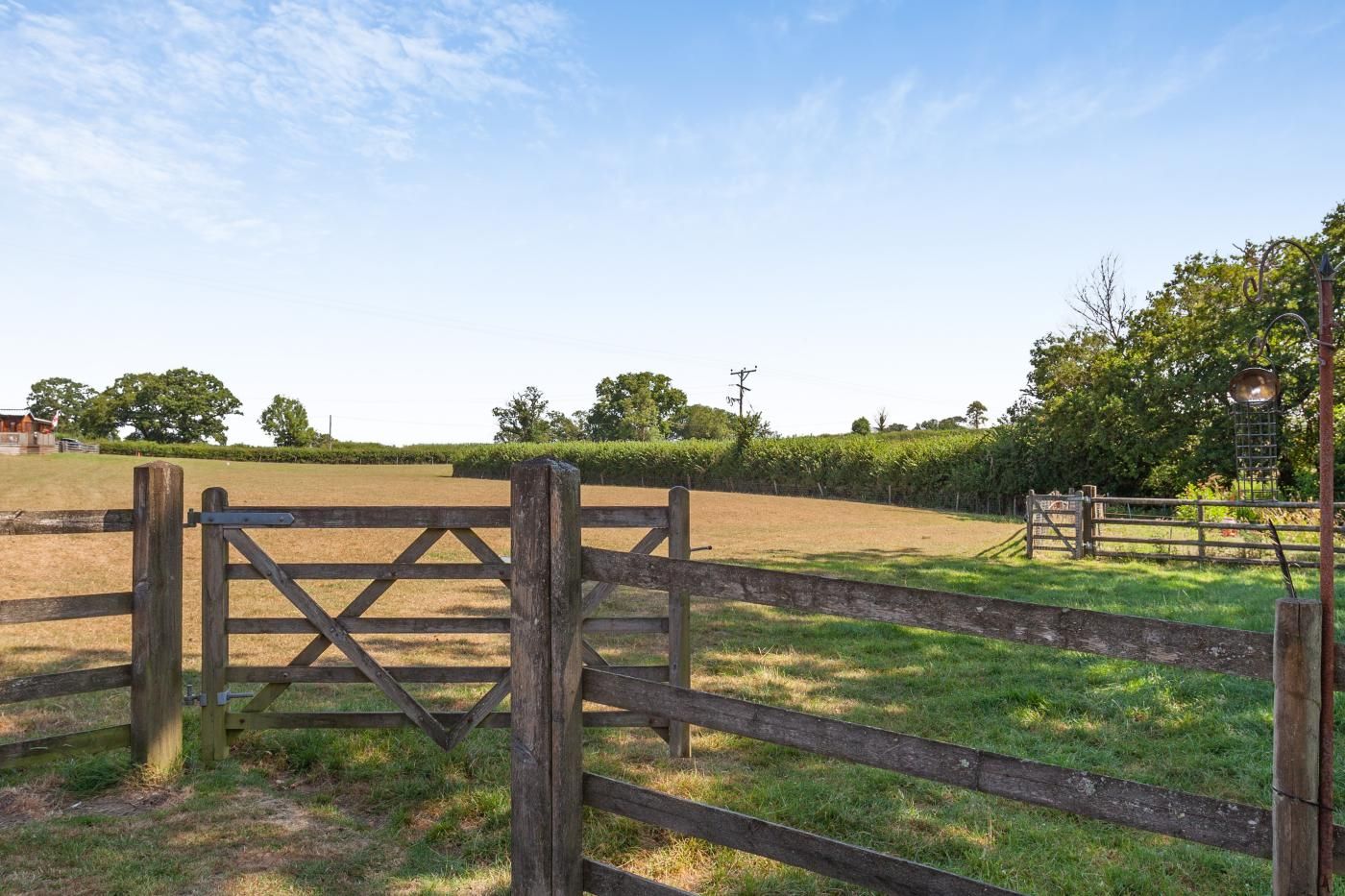 A wooden gate leading to a grassy field with a fence and trees in the background.