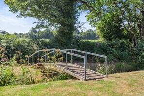 A wooden bridge with metal railings in a lush, green park setting.
