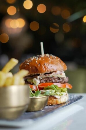 Un hamburger garni de laitue, de tomates et servi dans un pain aux graines de sésame, accompagné d’une petite portion de frites.