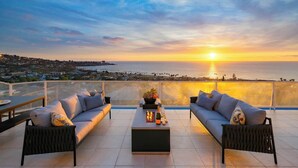 En tagterrasse med en sofasæt, et sofabord og havudsigt i solnedgang.