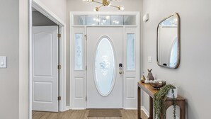 A hallway with a white door, a wooden console table with decorative items, and a mirror on the wall. - Family & Pet Friendly, New Plunge Pool & Grill, No Stairs,Walk 2 Beach,Sleeps 12 (Destin)