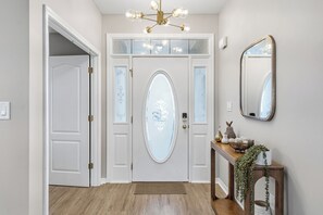 A hallway with a white door, a wooden console table with decorative items, and a mirror on the wall. - Family & Pet Friendly, New Plunge Pool & Grill, No Stairs,Walk 2 Beach,Sleeps 12 (Destin)
