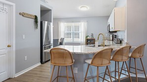 A kitchen with a central island, bar stools, a refrigerator, and a window with blinds. - Family & Pet Friendly, New Plunge Pool & Grill, No Stairs,Walk 2 Beach,Sleeps 12 (Destin)
