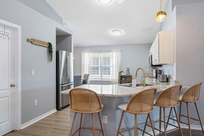 A kitchen with a central island, bar stools, a refrigerator, and a window with blinds. - Family & Pet Friendly, New Plunge Pool & Grill, No Stairs,Walk 2 Beach,Sleeps 12 (Destin)