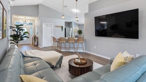 A modern living room with a sectional sofa, a round coffee table, and a dining area with a kitchen in the background. - Family & Pet Friendly, New Plunge Pool & Grill, No Stairs,Walk 2 Beach,Sleeps 12 (Destin)