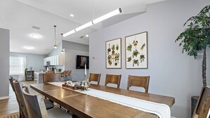 A dining area with a long wooden table, chairs, a white table runner, and two framed botanical prints on the wall. - Family & Pet Friendly, New Plunge Pool & Grill, No Stairs,Walk 2 Beach,Sleeps 12 (Destin)