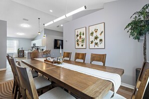 A dining area with a long wooden table, chairs, a white table runner, and two framed botanical prints on the wall. - Family & Pet Friendly, New Plunge Pool & Grill, No Stairs,Walk 2 Beach,Sleeps 12 (Destin)