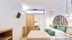 Une chambre à coucher comprenant un lit, une armoire en bois, une petite table, un téléviseur fixé au mur et un luminaire au plafond.