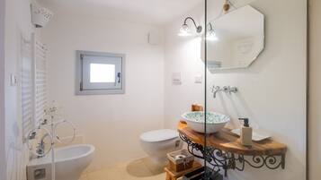 A bathroom with a white sink, a white toilet, a bidet, a mirror, and a small window.