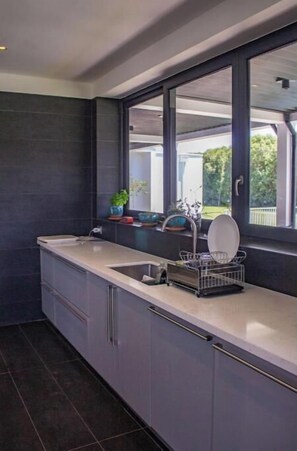 A modern kitchen with a large window, dark tiles, and a dish rack.
