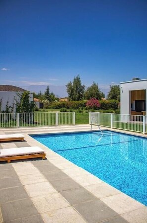 A swimming pool with a white fence, lounge chairs, and a view of the surrounding landscape.