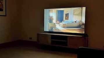 Une pièce avec un téléviseur posé sur un meuble en bois, un sol recouvert d’une moquette et un tableau encadré accroché au mur.