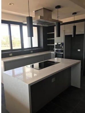 A modern kitchen with a central island, built-in oven, and pendant lighting.