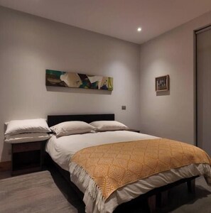 A bedroom with a bed, pillows, a headboard, a wall-mounted painting, and a door.