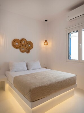A modern bedroom with a bed, white bedding, a hanging light fixture, and a window. - Victoria s Relax House (Paros)