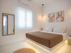 A modern bedroom with a bed, a mirror, a window with blinds, and wall art. - Victoria s Relax House (Paros)