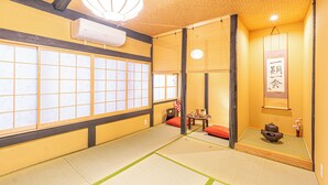 Ein traditioneller japanischer Raum mit Tatami-Böden, Schiebetüren, einem Tisch aus Tatami-Matten, einer hängenden Leuchte und einer Wand-Klimaanlage.