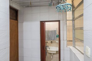 A bathroom with a white sink, a wooden door, and a window with blinds. - Leme 2 quartos amplo 2 min praia (Rio de Janeiro)