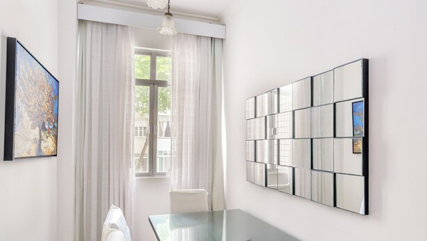 Une pièce moderne avec une table à manger en verre, des rideaux blancs et un grand miroir au mur.