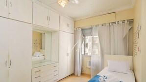Une chambre à coucher avec un lit, une armoire, un miroir et une fenêtre avec des rideaux.