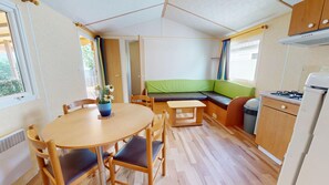 A compact kitchen with a dining area, a small seating area, and a window with curtains. - Le Bois Perdu (Saint-Jean-de-Monts)
