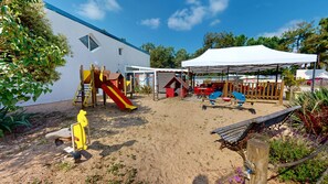 A sandy outdoor play area with a slide, climbing structures, and a covered seating area. - Le Bois Perdu (Saint-Jean-de-Monts)