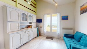 Una habitació amb un armari blanc, un sofà color turquesa, una televisió i una finestra amb vistes.