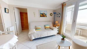 A cozy room with a sofa, a small table, a chair, a potted plant, and a view of the outside. - Chaloupe - Direct sea view 50m from the beach (Saint-Hilaire-de-Riez)