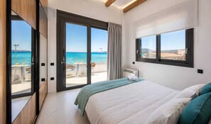 Une chambre avec un lit, une fenêtre, une vue sur la mer et un balcon avec des sièges d’extérieur.