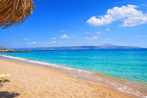 Una playa con aguas turquesas cristalinas, una orilla arenosa y una cadena montañosa distante.