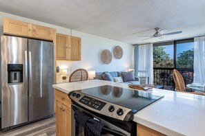 Una cocina moderna con refrigerador de acero inoxidable, placa de inducción, armarios de madera y un comedor con vistas.