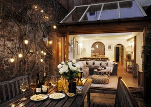 An outdoor dining area with a table set for a meal, a glass of wine, and a bottle of wine. - Dolls House - Luxury Townhouse (Henley-on-Thames)