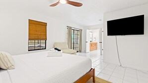 Un dormitorio con cama, ventilador de techo, televisión, ventana con cortinas y vistas a una puerta y un armario.