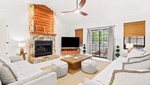 Una sala de estar con chimenea de piedra, un televisor de pantalla plana, una mesa de centro de madera y un ventilador de techo.
