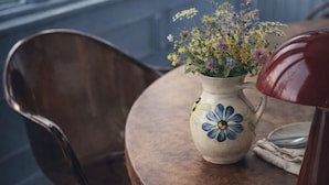 A wooden chair, a table with a vase of flowers, and a lamp.