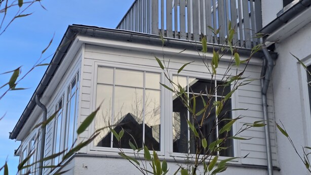 A building with a balcony, windows, and a reflection in the glass.