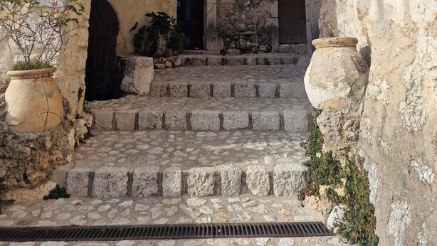 Un portail en pierre en arc de cercle mène à une cour intérieure dotée d’un escalier, d’un pot de fleurs et d’un élément décoratif en forme d’étoile placé au-dessus.