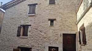 Un bâtiment en pierre doté de nombreuses fenêtres, une porte ornée d’une guirlande décorative et un petit jardin avec des plantes en pot.