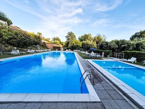 A rectangular swimming pool with a tiled deck, surrounded by lounge chairs and umbrellas. - Lake and Pool by Interhome (Leggiuno)