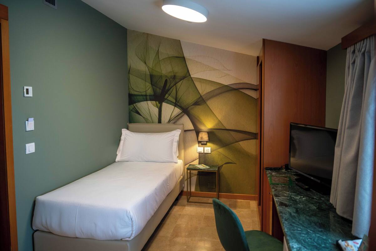 Habitación de hotel con cama, televisión, una mesita con lámpara y un mural en la pared.